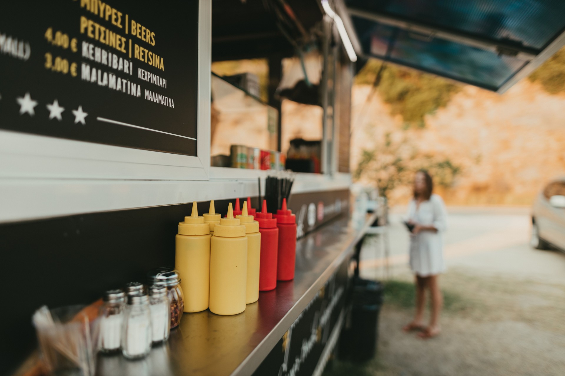 Condiments in yellow and red squeeze bottles on food truck counter, with menu board featuring local food and beverage options, emphasizing Bronx Local SEO services for enhancing business visibility.