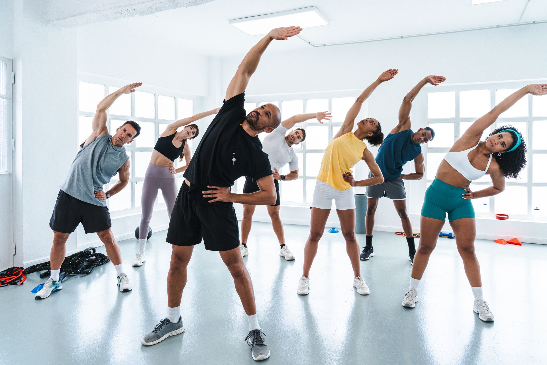 Group of diverse individuals participating in a fitness class, performing side stretches in a bright studio, emphasizing health and community engagement.